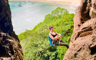 Rock climber scaling cliffs at Railay Beach, Krabi with ocean view in background.