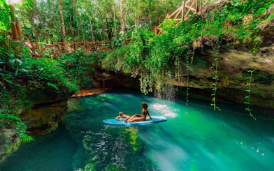 Visitors paddleboarding in a lush cenote, Cancun Extreme Adventure.
