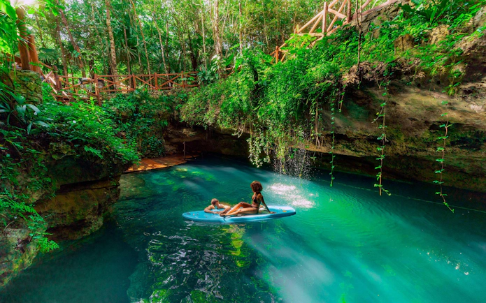 Visitors paddleboarding in a lush cenote, Cancun Extreme Adventure.