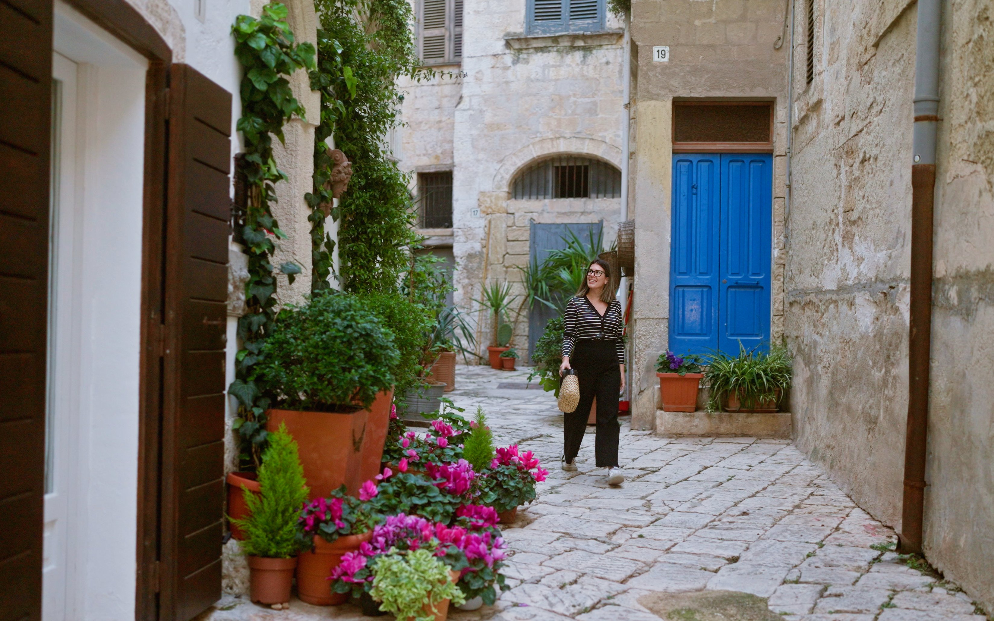 Woman walking through a narrow street with colorful flowers in Polignano a Mare, Puglia, Italy.