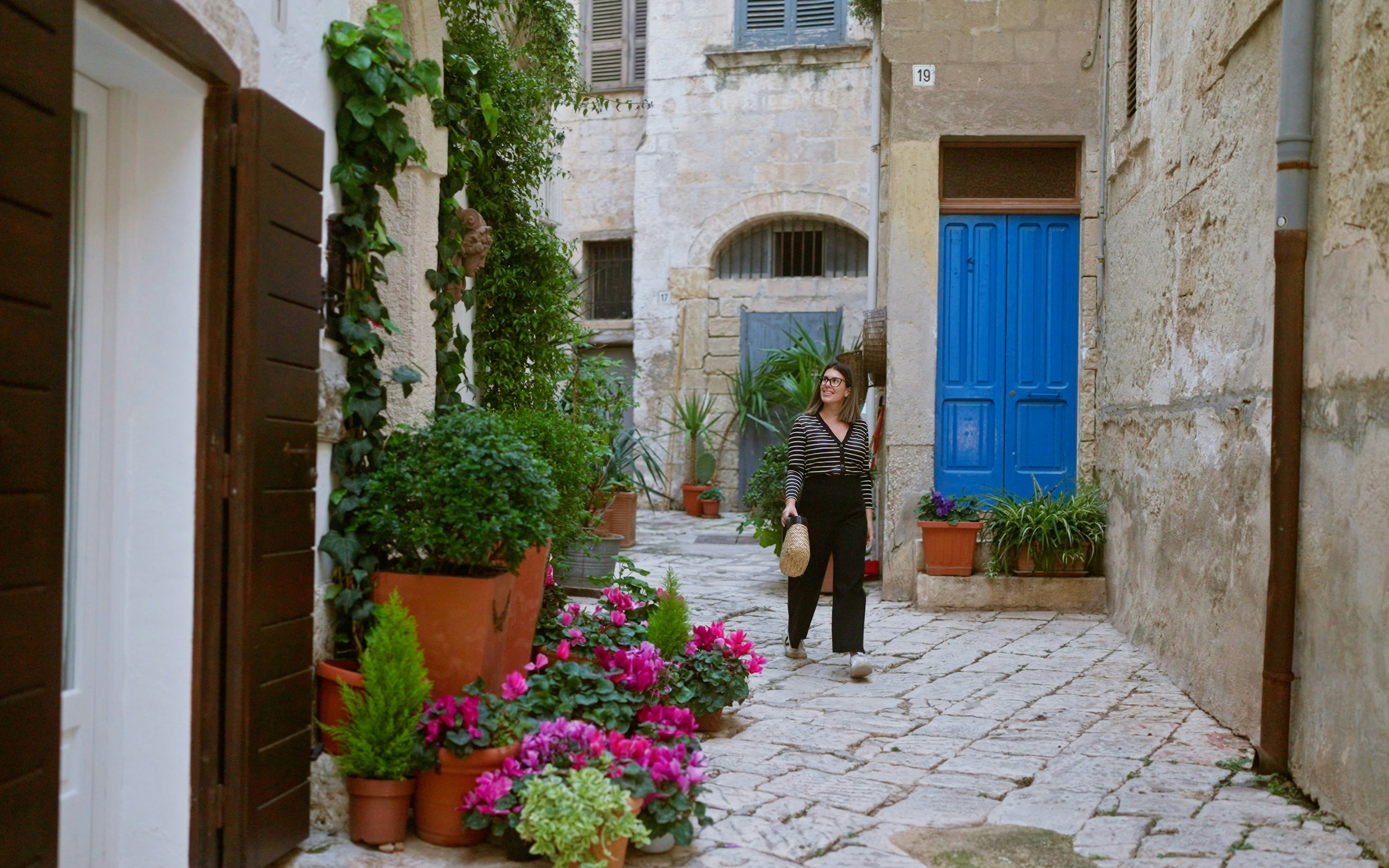 Woman walking through a narrow street with colorful flowers in Polignano a Mare, Puglia, Italy.
