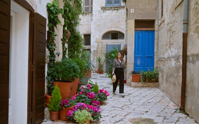Woman walking through a narrow street with colorful flowers in Polignano a Mare, Puglia, Italy.