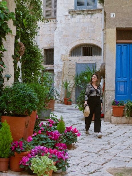 Woman walking through a narrow street with colorful flowers in Polignano a Mare, Puglia, Italy.