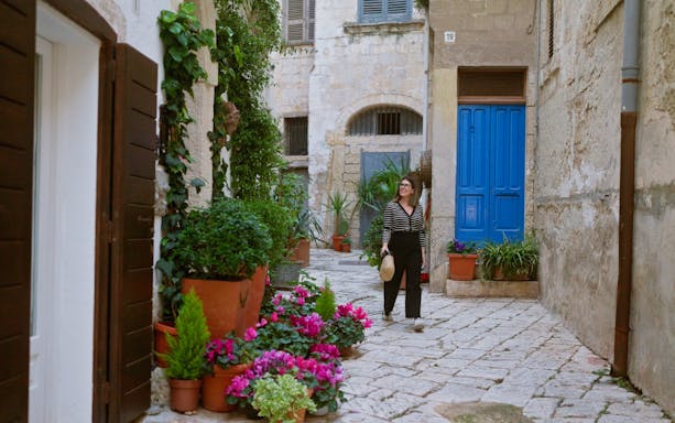 Woman walking through a narrow street with colorful flowers in Polignano a Mare, Puglia, Italy.