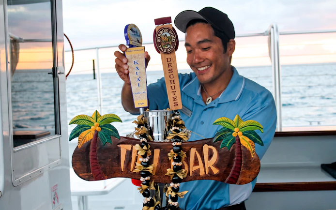 Bartender serving drinks on Waikiki Signature Sunset Sail with ocean view.