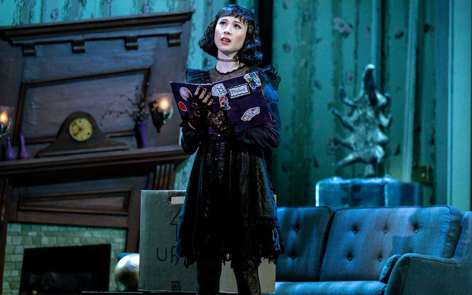 Performer on stage during Beetlejuice show in Brisbane, holding a book in a living room set.