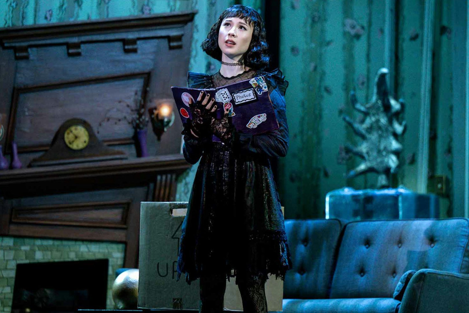 Performer on stage during Beetlejuice show in Brisbane, holding a book in a living room set.