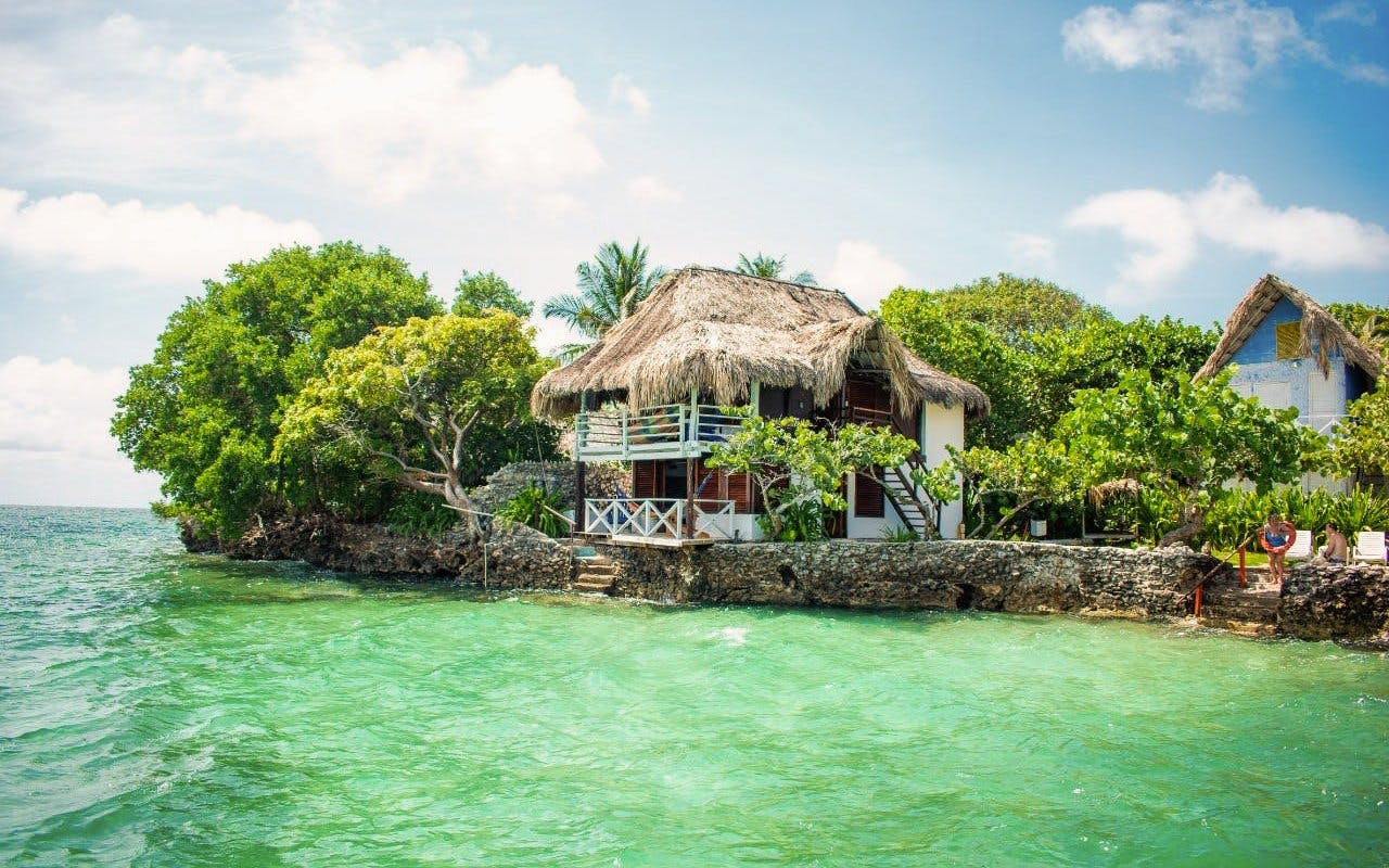 Thatch-roofed hut on Isla del Pirata, Rosario Islands, surrounded by lush greenery and turquoise water.