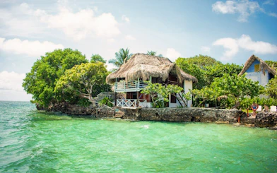 Thatch-roofed hut on Isla del Pirata, Rosario Islands, surrounded by lush greenery and turquoise water.