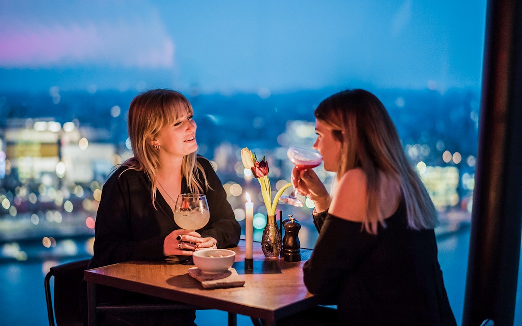 Two people enjoying drinks at a table with a city view at ADAM Lookout, Amsterdam.