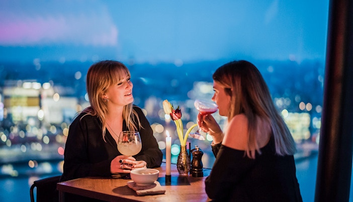 Two people enjoying drinks at a table with a city view at ADAM Lookout, Amsterdam.