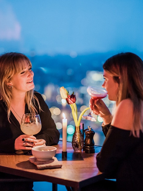 Two people enjoying drinks at a table with a city view at ADAM Lookout, Amsterdam.