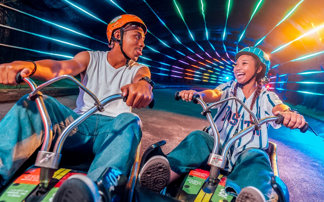 Friends enjoying night luge ride with colorful lights in Singapore.