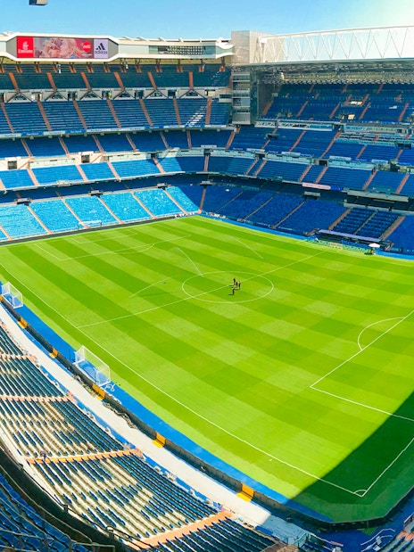 Santiago Bernabeu stadium view from stand, showcasing empty seats and green pitch.