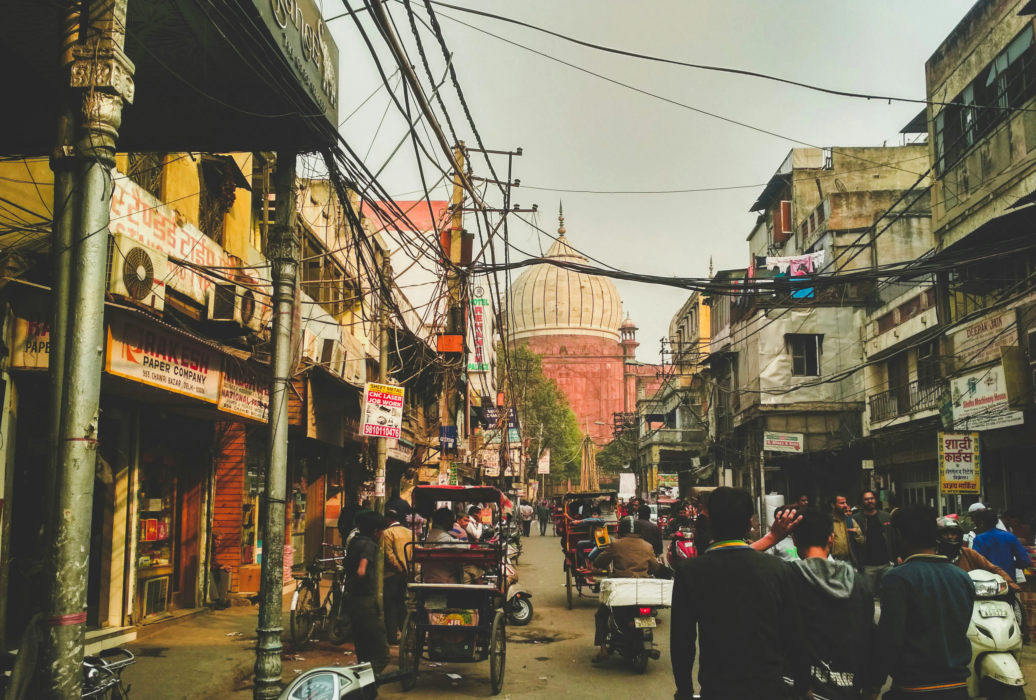 Bustling Jaipur street with shops and rickshaws, featuring a historic dome in the background.