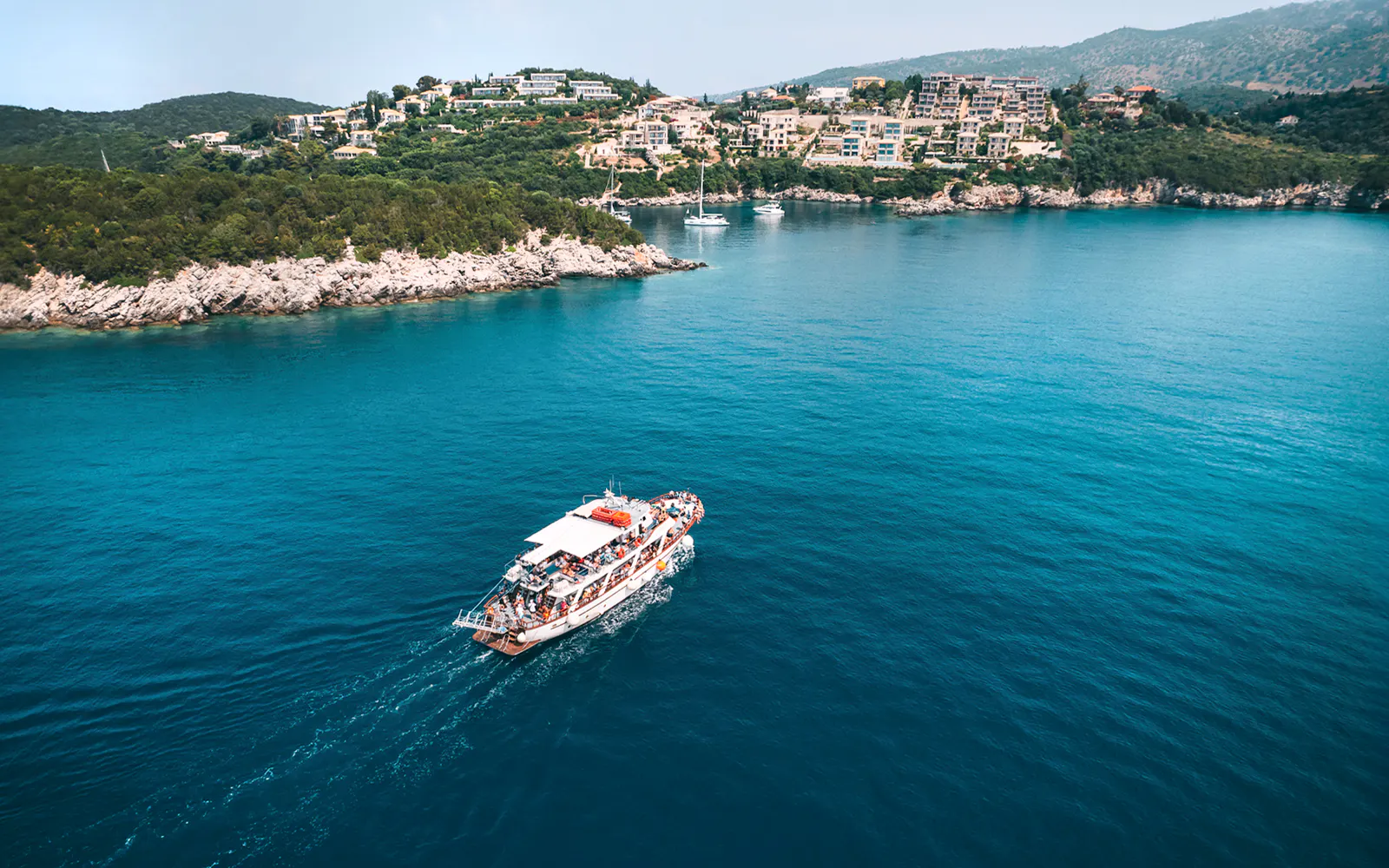 Cruise boat on Blue Lagoon waters near Benitses, Corfu, with coastal view.