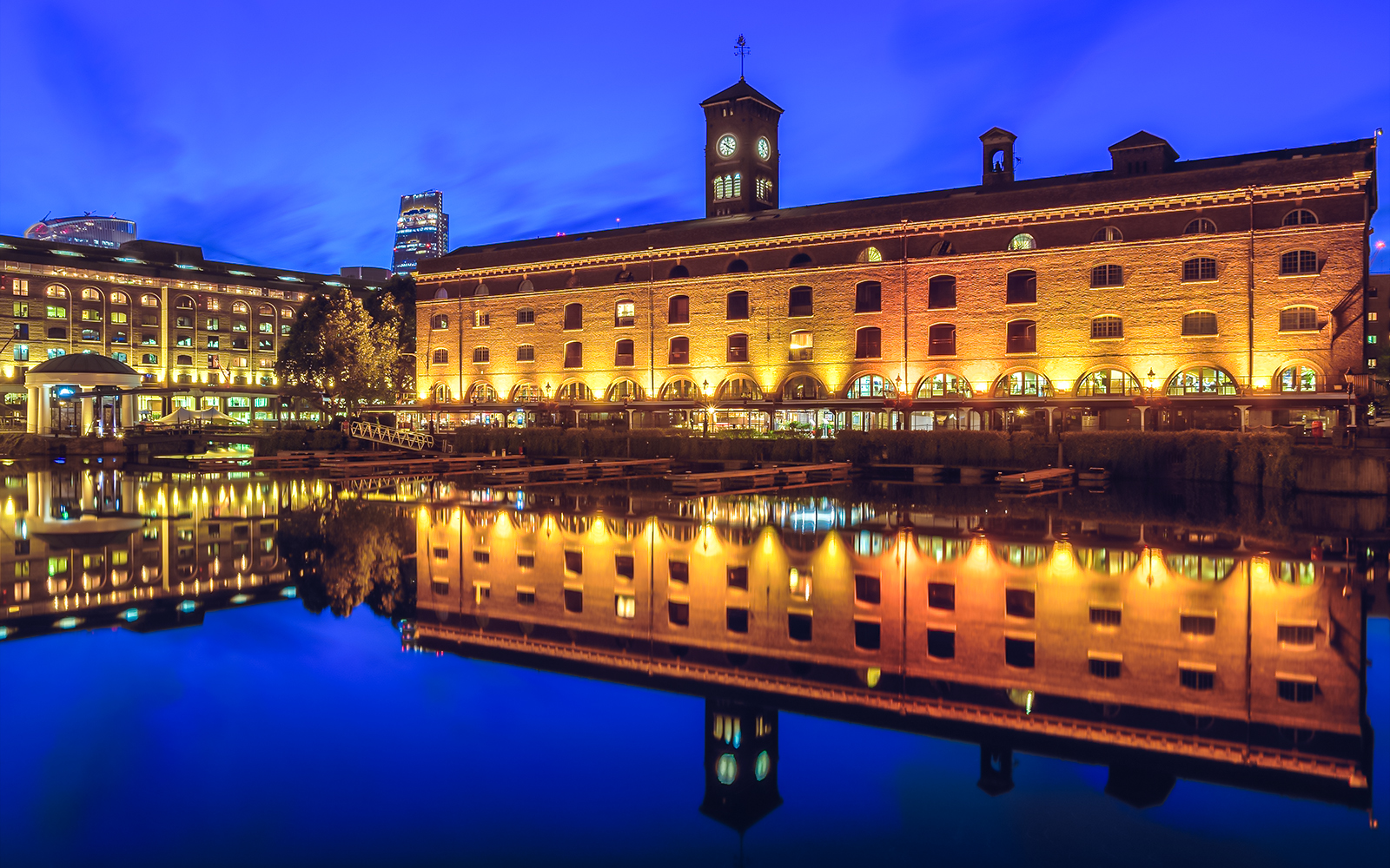 St Katharine Docks in London illuminated at night with reflections on the water.
