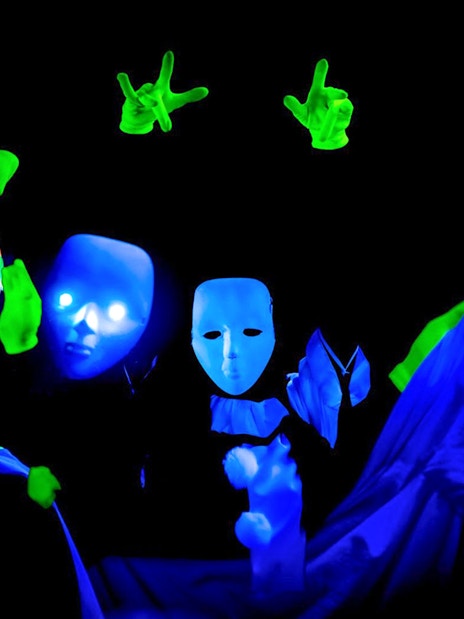 Performers with masks and gloves in Prague black light theatre.
