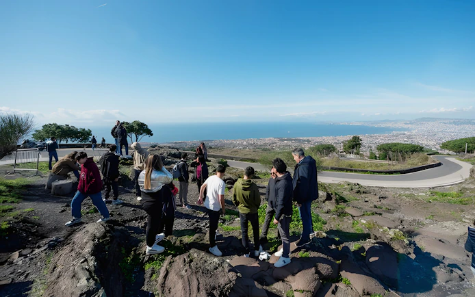 Group hiking at Vesuvius National Park with view of Naples, Italy in the background.