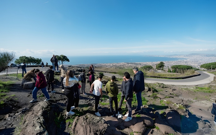 Group hiking at Vesuvius National Park with view of Naples, Italy in the background.