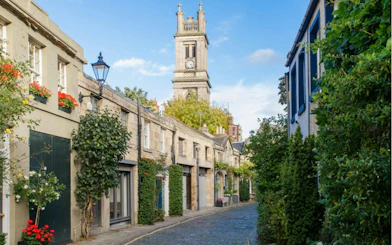 Cobblestone street with historic buildings and clock tower in Edinburgh.