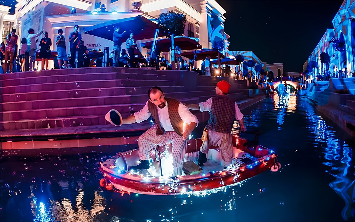 Boat parade at Land of Legends Night Show with performers on illuminated canal.