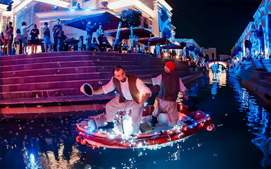 Boat parade at Land of Legends Night Show with performers on illuminated canal.