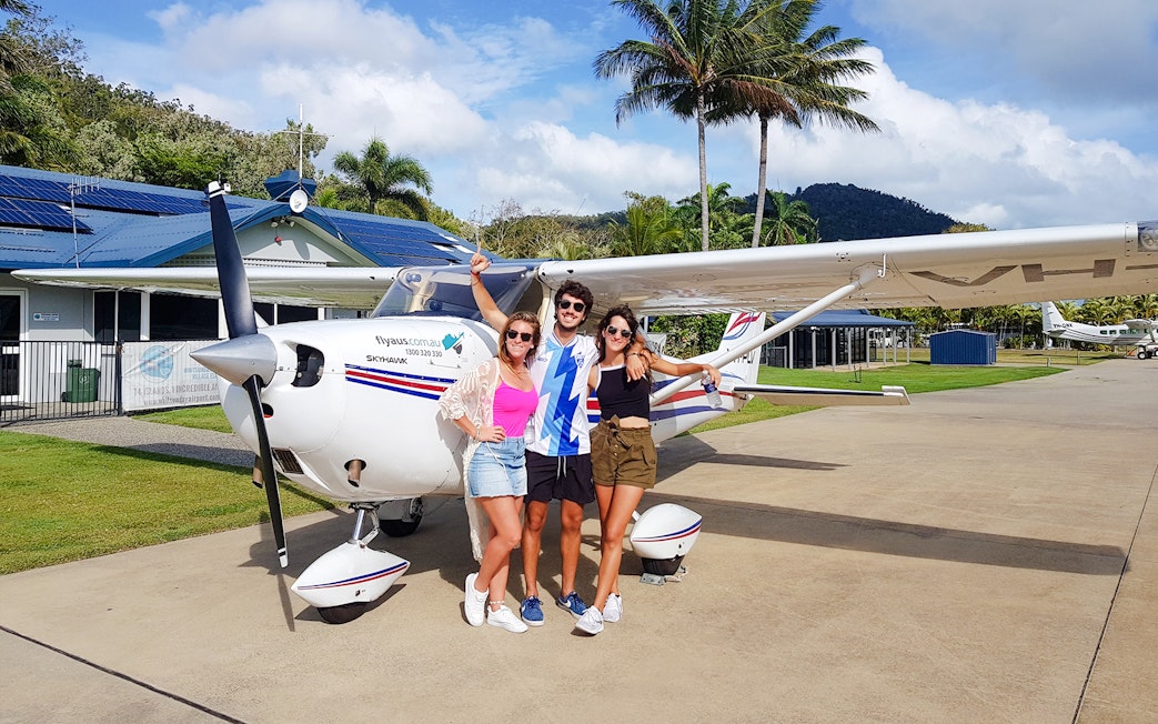 Group posing in front of small plane at tropical airstrip.