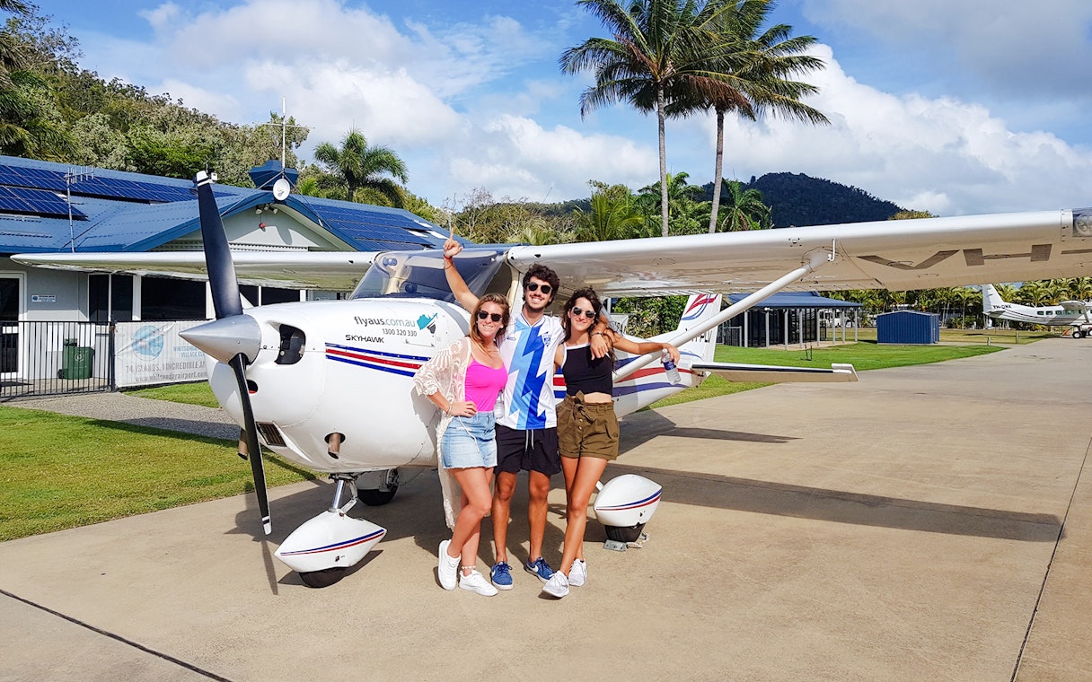 Group posing in front of small plane at tropical airstrip.