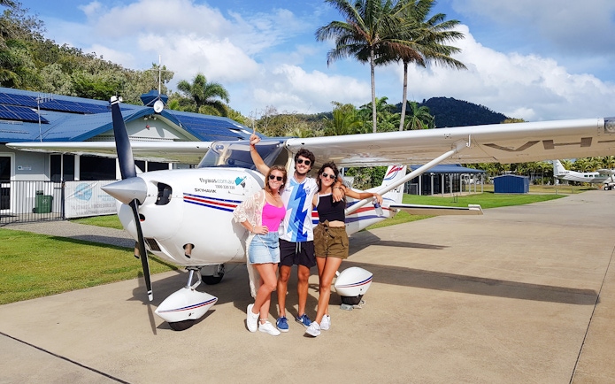 Group posing in front of small plane at tropical airstrip.