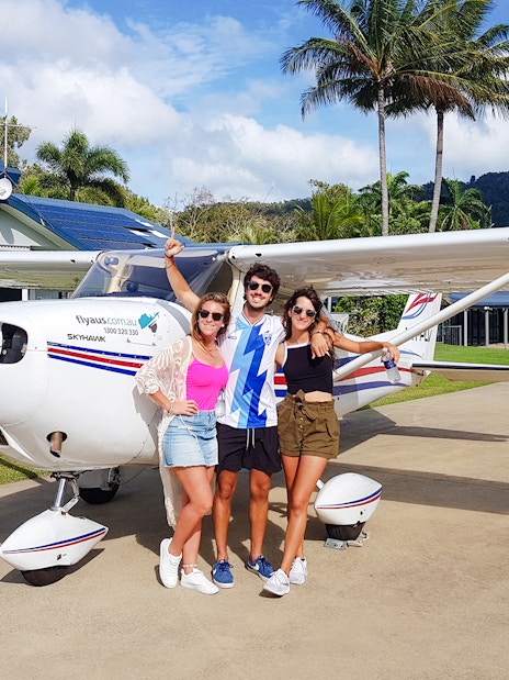 Group posing in front of small plane at tropical airstrip.