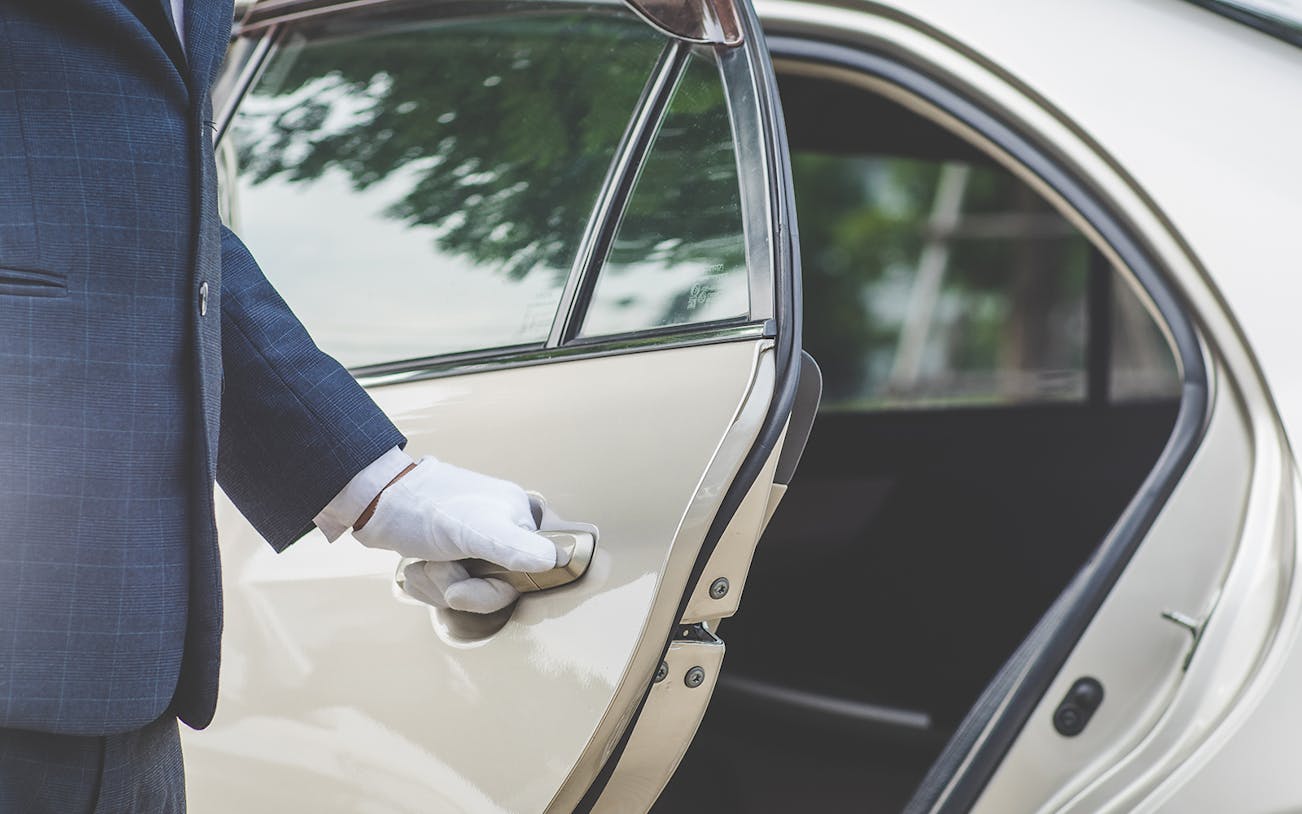 Chauffeur opening car door for private airport transfer in Bangkok.