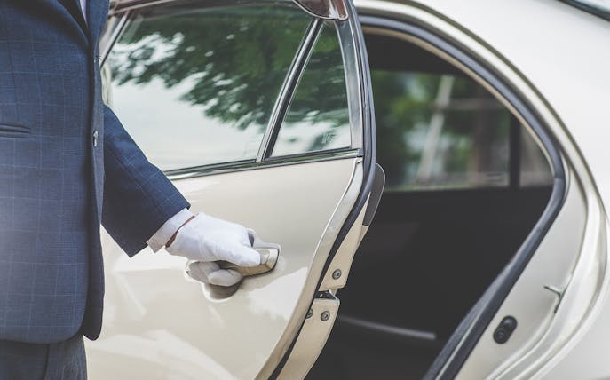 Chauffeur opening car door for private airport transfer in Bangkok.