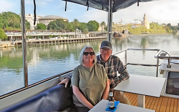Tourists enjoying a cruise on the Guadalquivir River in Seville with Torre del Oro in view.