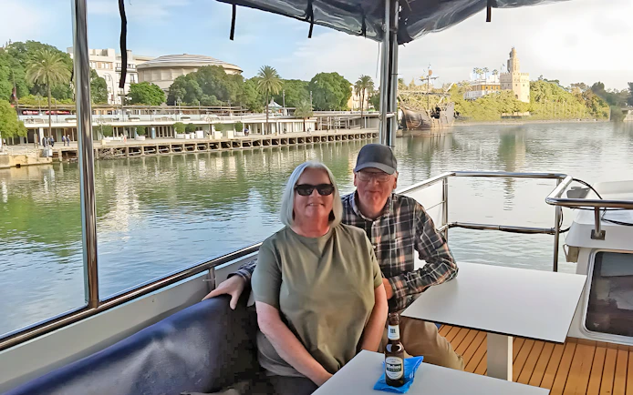 Tourists enjoying a cruise on the Guadalquivir River in Seville with Torre del Oro in view.