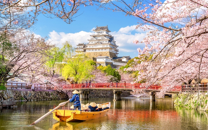 Osaka Castle with cherry blossoms and a boat on the moat, skip-the-line tickets available.