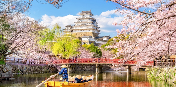 Osaka Castle with cherry blossoms and a boat on the moat, skip-the-line tickets available.