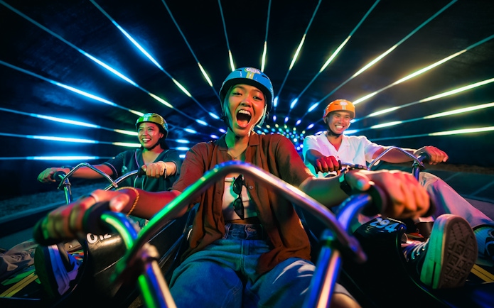 Friends enjoying night luge ride in illuminated tunnel, Singapore.
