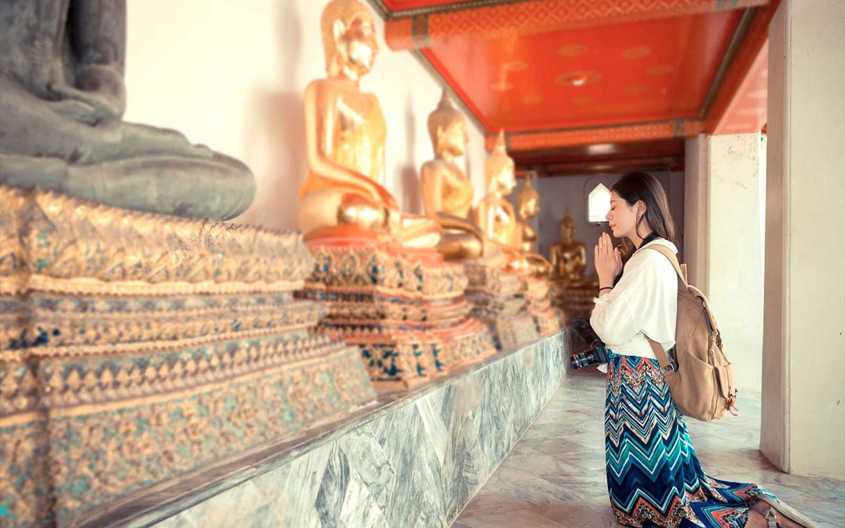 Visitor praying beside Buddha statues at Grand Palace, Bangkok.