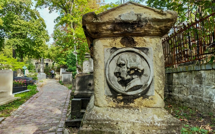 Tombstone with carved portrait along cobblestone path in Père Lachaise Cemetery, Paris.