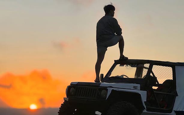 Person standing on a 4WD jeep at sunset in Kintamani.