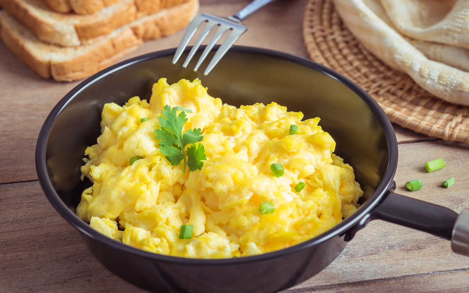 Scrambled eggs with peas and corriander on top served in a black bowl and fork