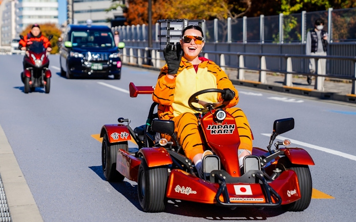 Person in tiger costume driving go-kart on Shibuya street, Tokyo.