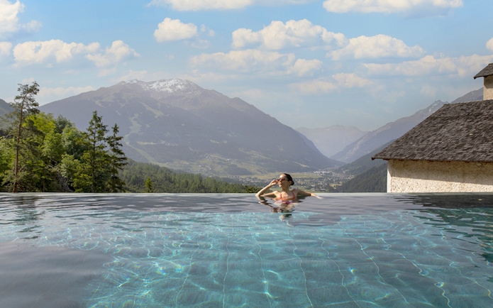 Person relaxing in an infinity pool with mountain views at QC Terme Bagni Vecchi di Bormio.