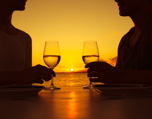 Couple toasting with wine glasses at sunset on Seine River cruise dinner.