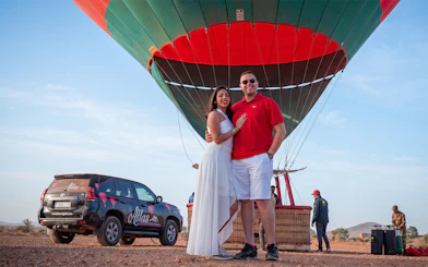 Couple standing in front of a hot air balloon in Marrakesh desert, ready for sunrise flight.