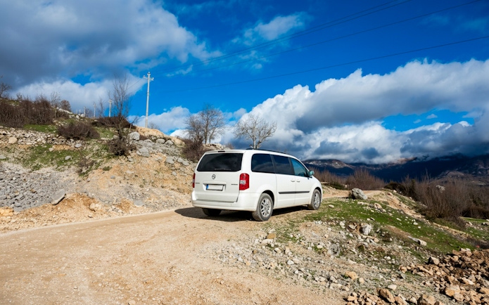 Minibus on a rural road with mountainous landscape in the background.