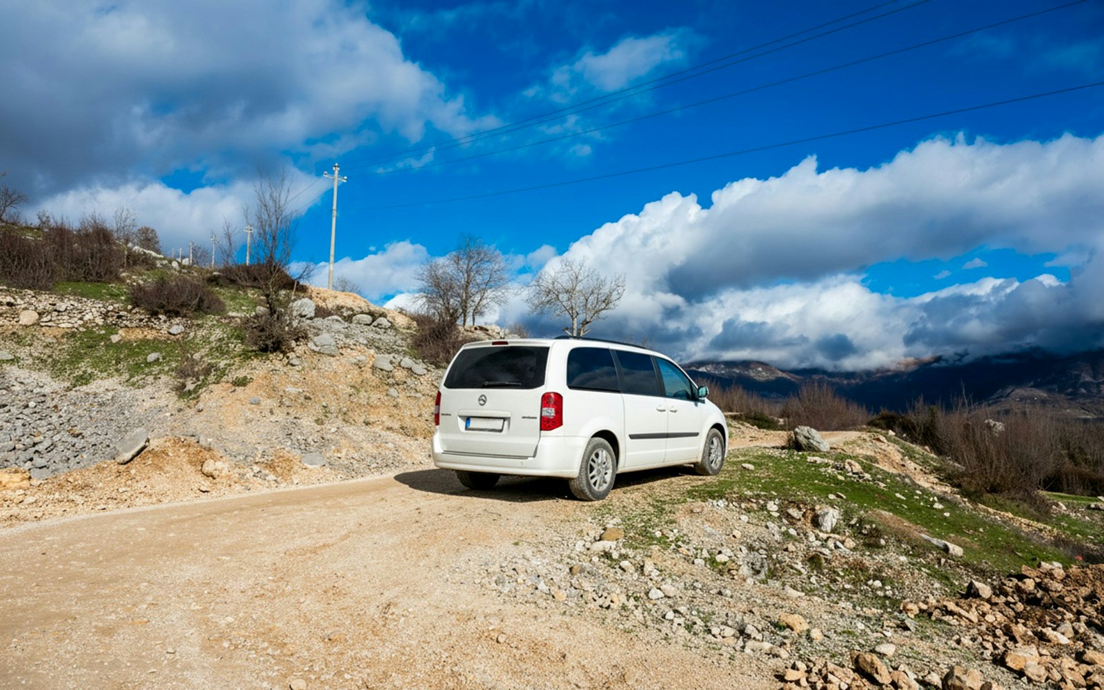 Minibus on a rural road with mountainous landscape in the background.