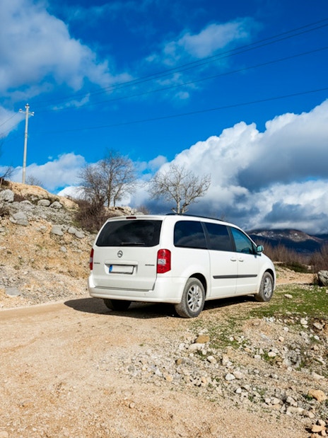 Minibus on a rural road with mountainous landscape in the background.