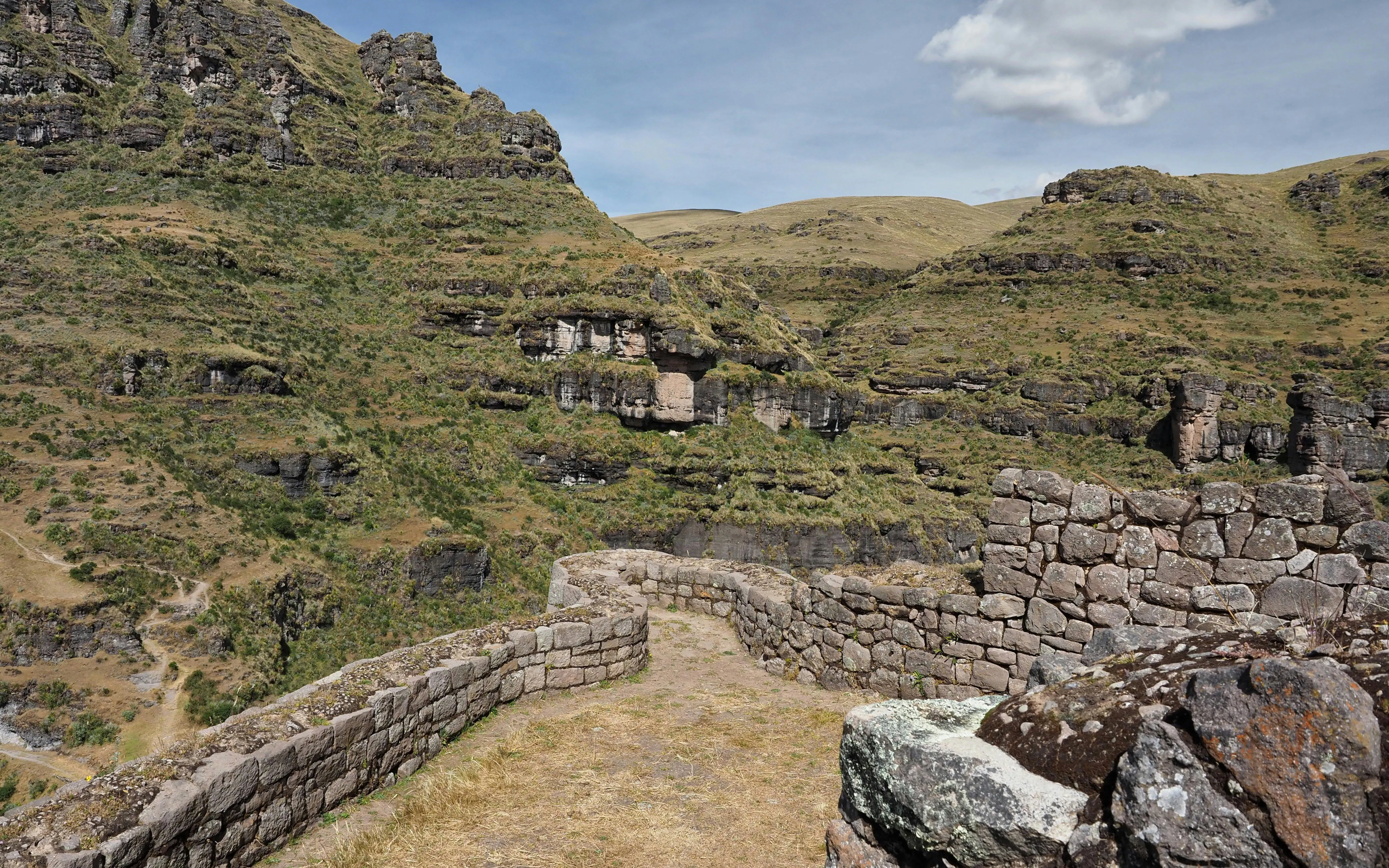 Stone walls of Waqrapukara archaeological site in Cusco, Peru, with mountainous landscape.